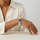 Pearl bracelet with a blue AB crystal floral center worn by a person in a cream shirt.