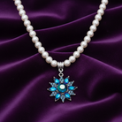 Faux pearl chain with a shiny blue floral pendant on a purple fabric background.