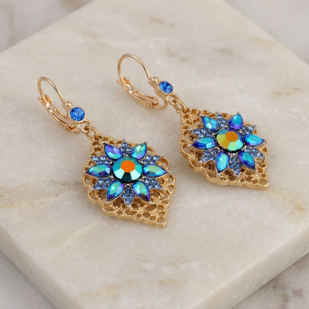 Antiqued Filigree Iridescent Blue AB Crystal & Sapphire Blue Stone Flower Drop Earrings resting on white marble stone
