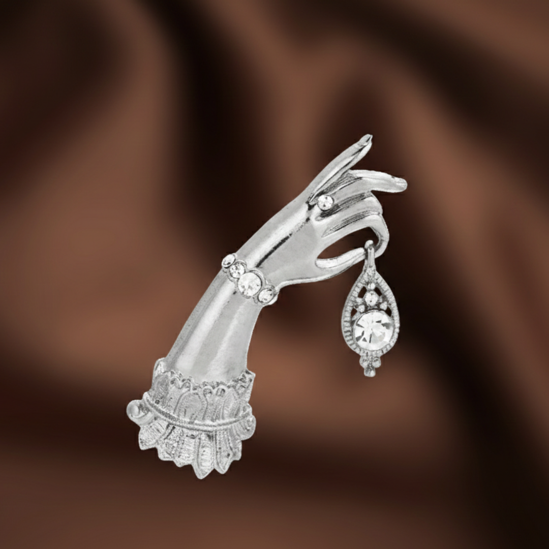 Silver hand-shaped brooch with gemstones on a brown background.