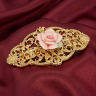 Decorative barrette with pink porcelain rose on a gold filigree setting against a red fabric background