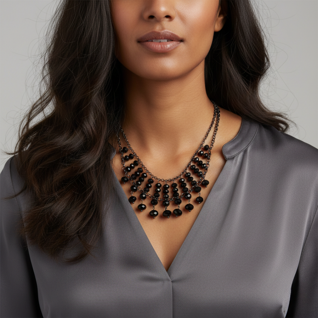 Woman wearing a black beaded necklace with a gray top against a neutral background