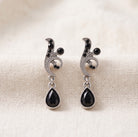 Antiquities Couture Black And Hematite Color Crystal Vine Drop Earrings on a beige linen background