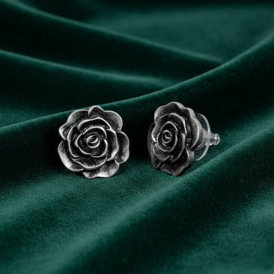 Silver rose-shaped earrings on a green fabric background