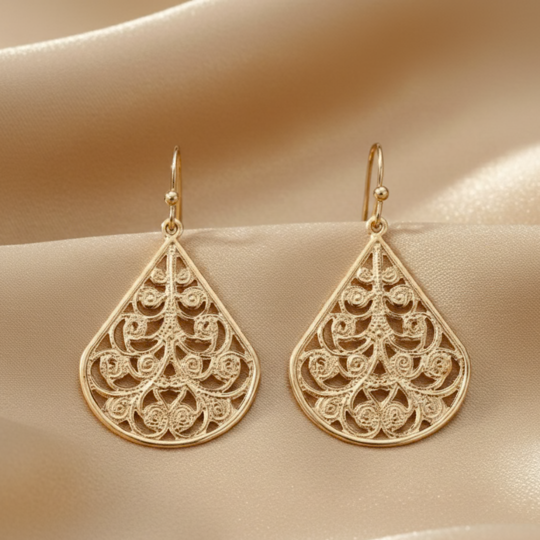 Gold earrings with intricate patterns on a beige fabric background
