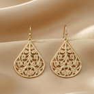 Gold earrings with intricate patterns on a beige fabric background