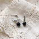 Antiquities Couture Black Drop Hoop Earrings resting on white laced vintage cloth