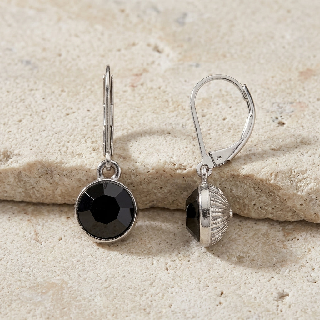 Classic Round Black Drop Earrings displayed on a textured beige stone surface.