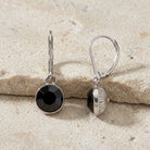 Classic Round Black Drop Earrings displayed on a textured beige stone surface.