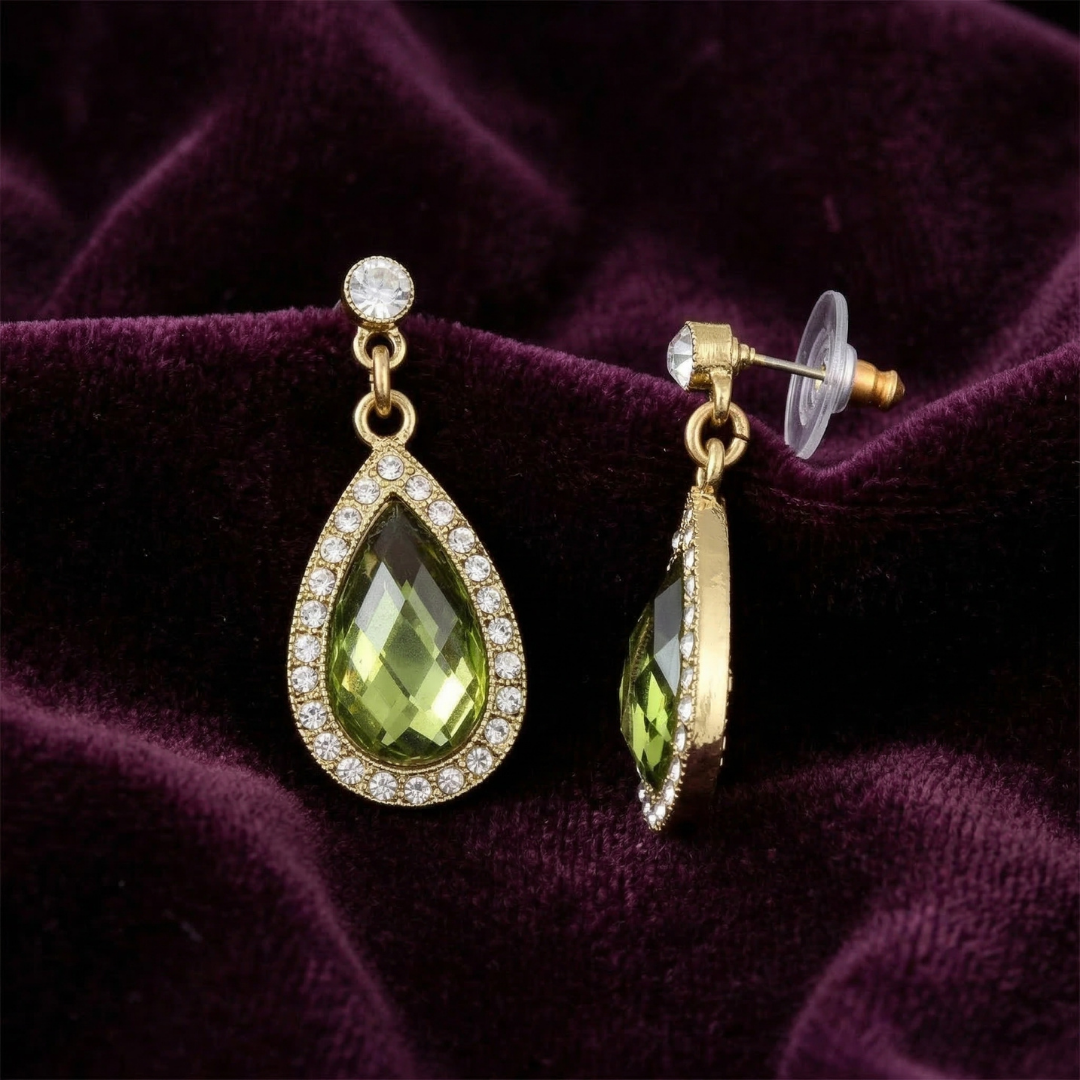 Gold earrings with green teardrop crystals on a purple fabric background