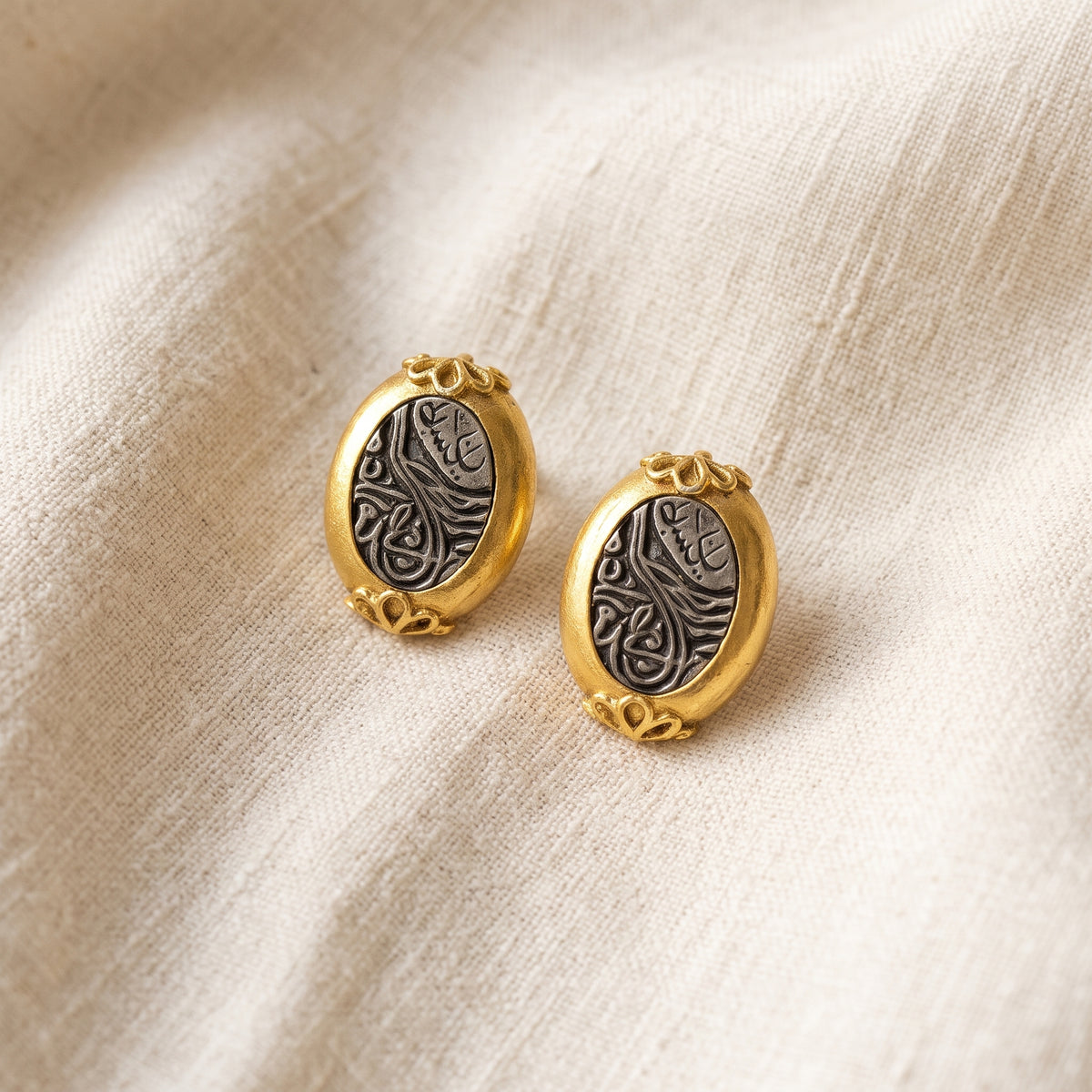 Gold and Pewter Tone Antiquities Couture Maharaja Script Oval Clip On Earrings resting on warm ivory linen