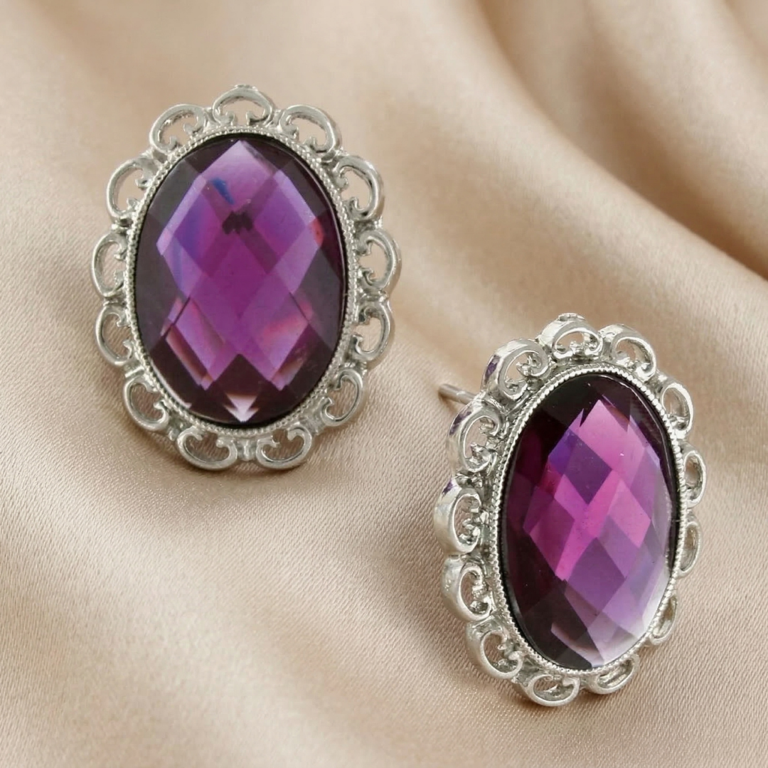 Pair of silver earrings with purple gemstones on a beige fabric background