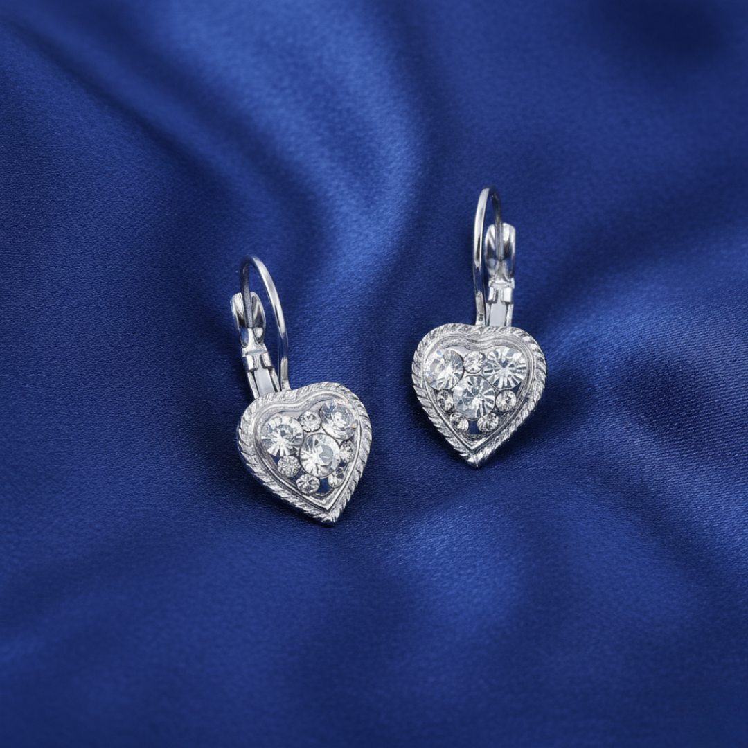 Heart-shaped silver earrings with clear crystals on a blue satin background