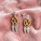 Antiquities Couture Two Tone Crystal 2 Drop Post Earrings displayed on a soft pink velvet fabric background.