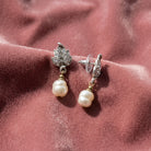 Antiquities Couture Crystal Baroque Faux Pearl Drop Post Earrings resting on pink fabric