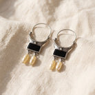 Antiquities Couture Venice Gondola Black Onyx Gemstone And Faux Pearl Hoop Dangle Earring resting on warm ivory linen