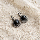 Black Oval Stone & Diamond Crystal Lever Back Earrings resting on a textured cream lace fabric.