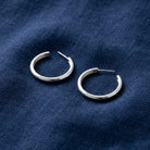 Silver Polished Classic Hoop Earrings resting on navy blue linen