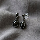 Petite Jet Black Stone Teardrop Post Dangle Earrings resting on gray linen fabric