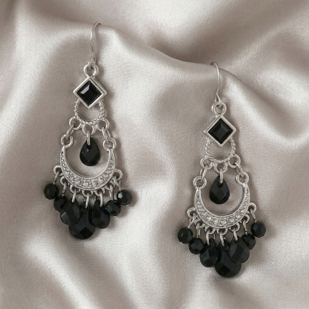 Pair of silver earrings with black beads on a beige fabric background