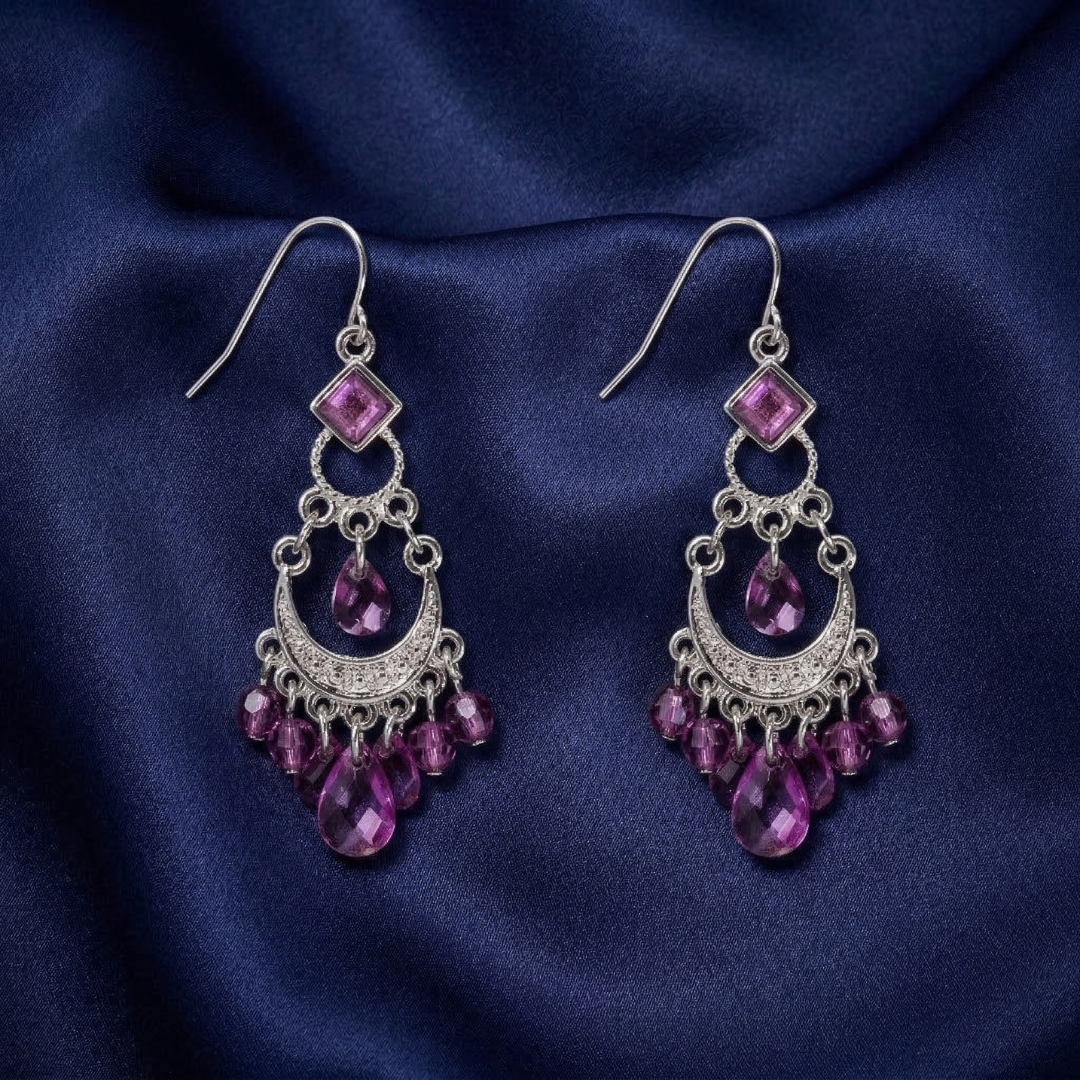 Pair of silver earrings with purple gemstones on a dark blue fabric background