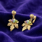 Gold-dipped leaf and grap earrings with multicolor beads on a purple fabric background