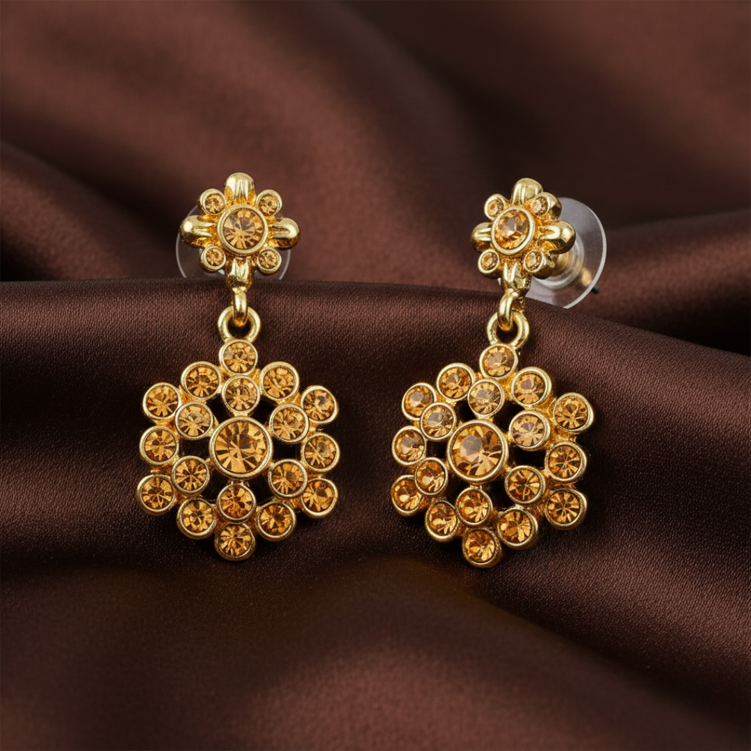 Gold earrings with brown crystals on a brown fabric background