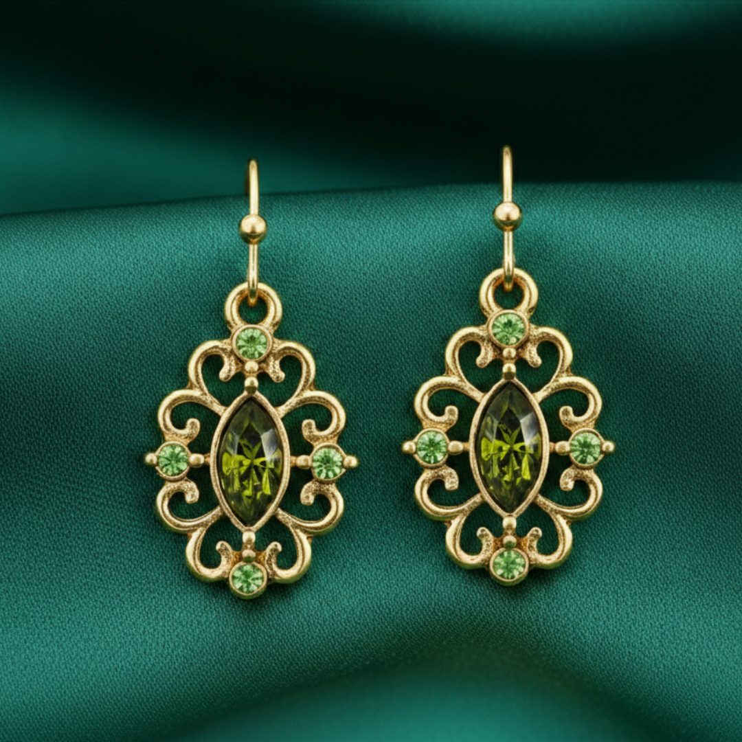 Gold earrings with green gemstones on a green fabric background
