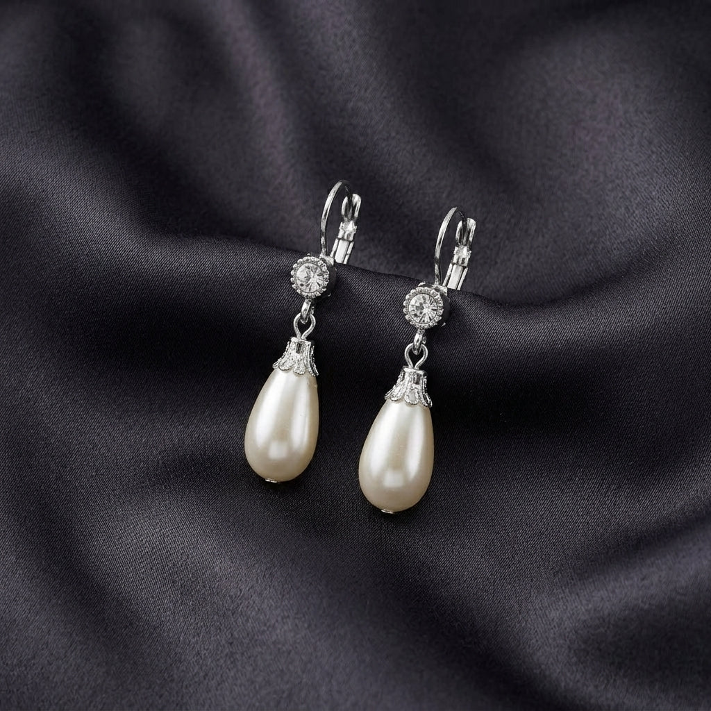 White faux pearl drop earrings with crystal accent resting on dark satin colored fabric