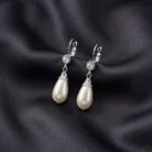 White faux pearl drop earrings with crystal accent resting on dark satin colored fabric