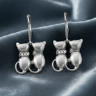 Silver cat-shaped earrings on a dark fabric background
