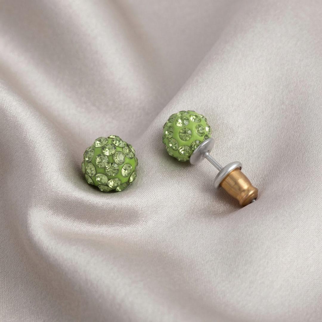 Green stud earrings with clear stones on a beige fabric background