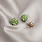 Green stud earrings with clear stones on a beige fabric background
