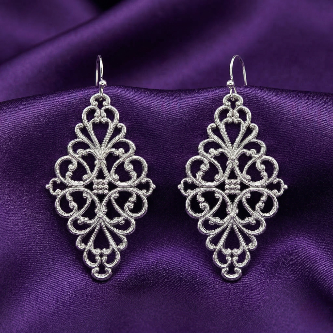Pair of silver filigree earrings on a purple fabric background