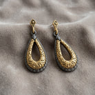 Antiquities Couture Two Tone Teardrop Earrings displayed on a textured greige fabric background.