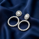 Faux pearl hoop earrings on a dark blue fabric background