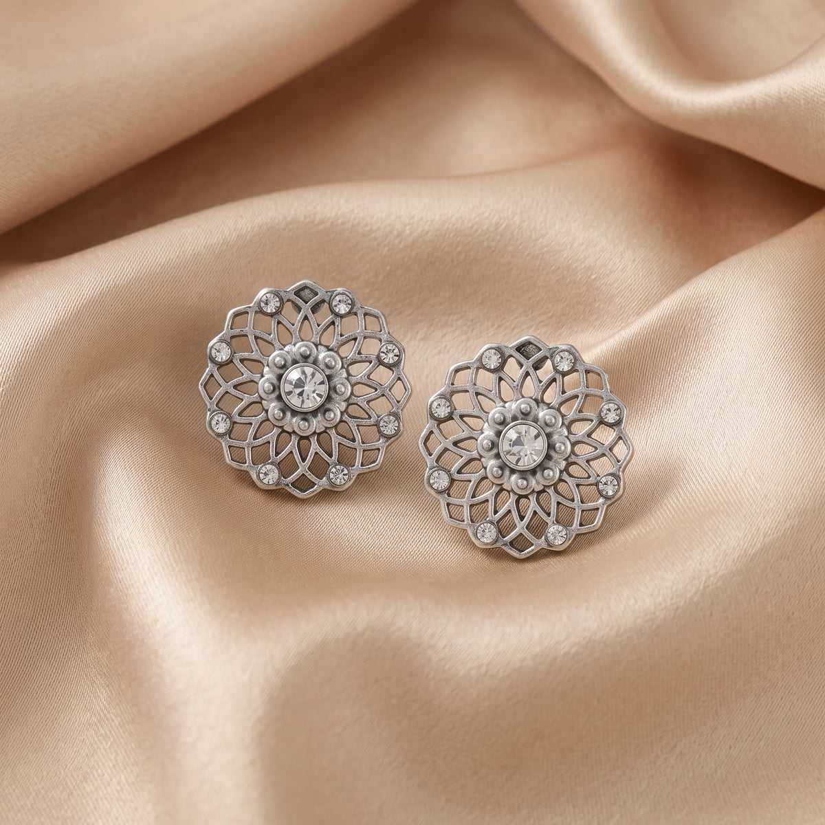 Crystal Filigree Large Button Earrings resting on champagne satin fabric