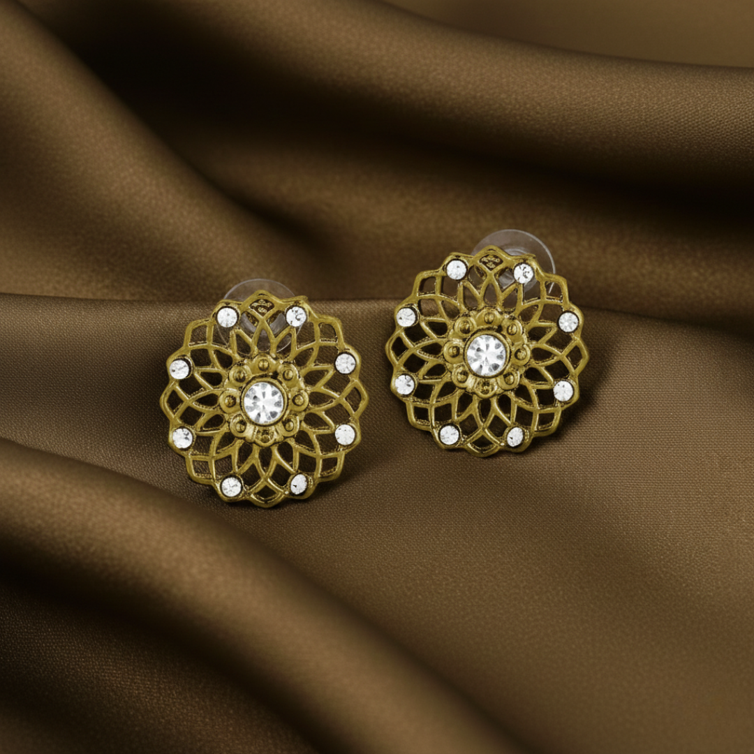 Gold floral earrings with clear stones on a brown fabric background.