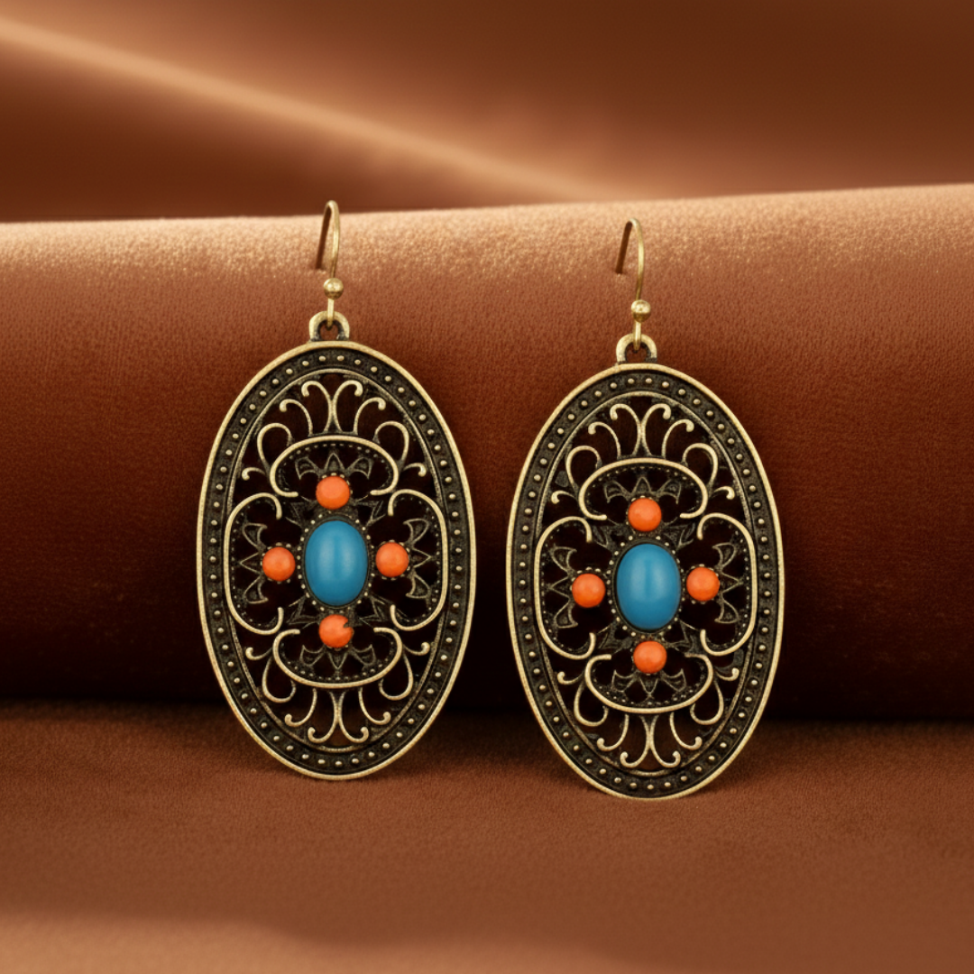 Ornate earrings with blue and orange stones on a brown fabric background
