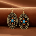 Ornate earrings with blue and orange stones on a brown fabric background