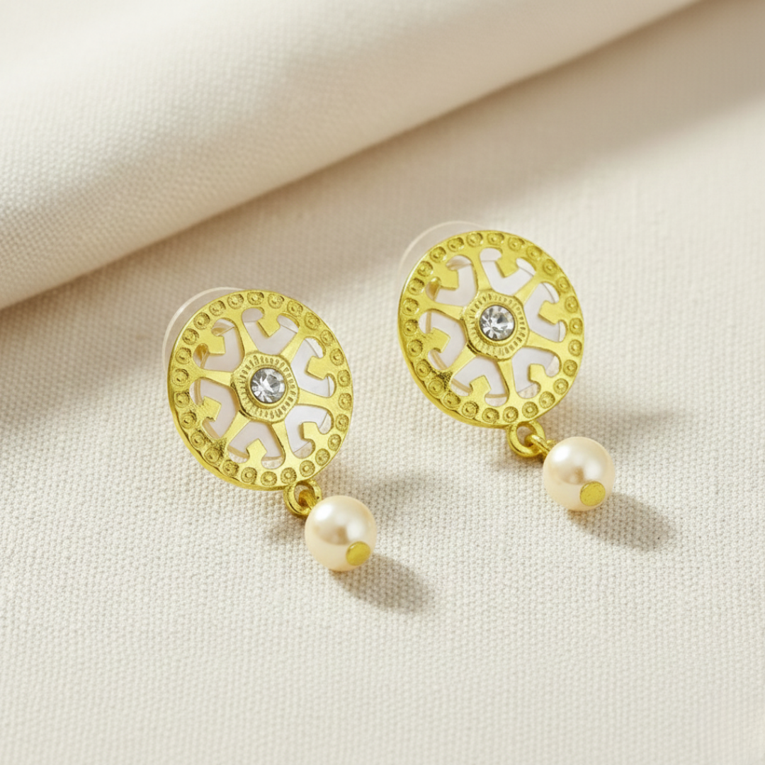 Gold earrings with faux pearl drops on a beige fabric background.