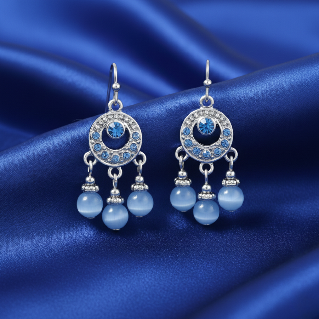 Pair of blue earrings with silver accents on a blue satin background