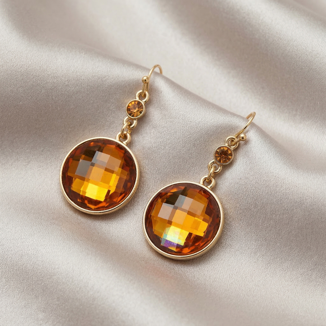 Gold earrings with topaz-colored gemstones on a beige fabric background