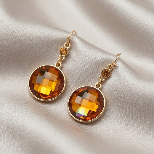 Gold earrings with topaz-colored gemstones on a beige fabric background