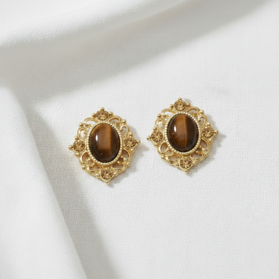 Gold earrings with brown gemstones on a white fabric background