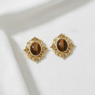 Gold earrings with brown gemstones on a white fabric background