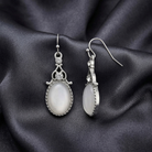 Pair of silver earrings with white stones on a dark fabric background