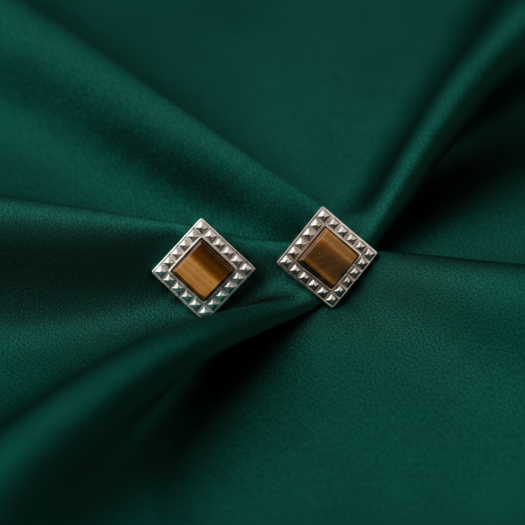 Pair of square earrings with brown centers on a green satin background