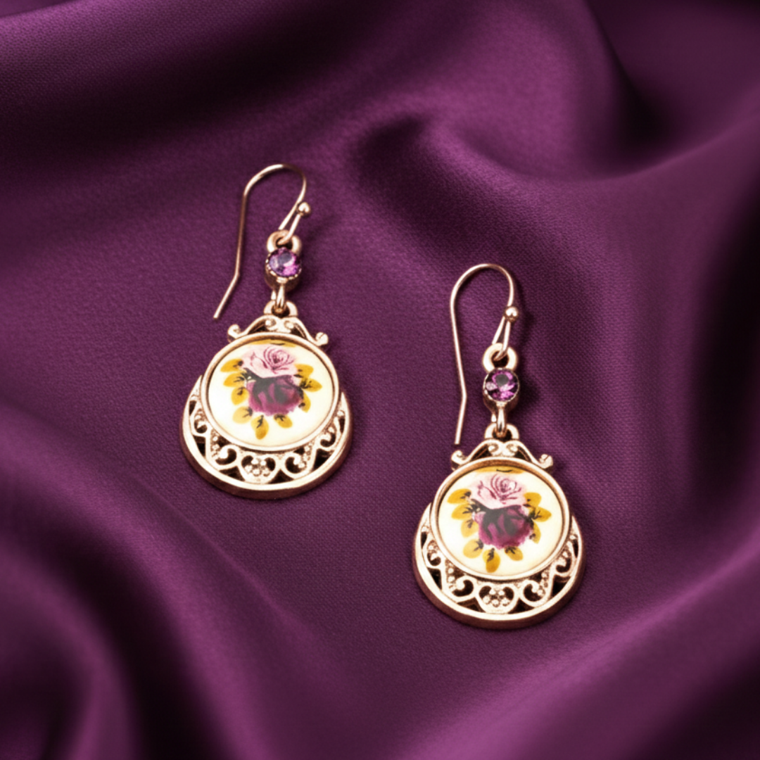Pair of gold earrings with floral designs on a purple fabric background