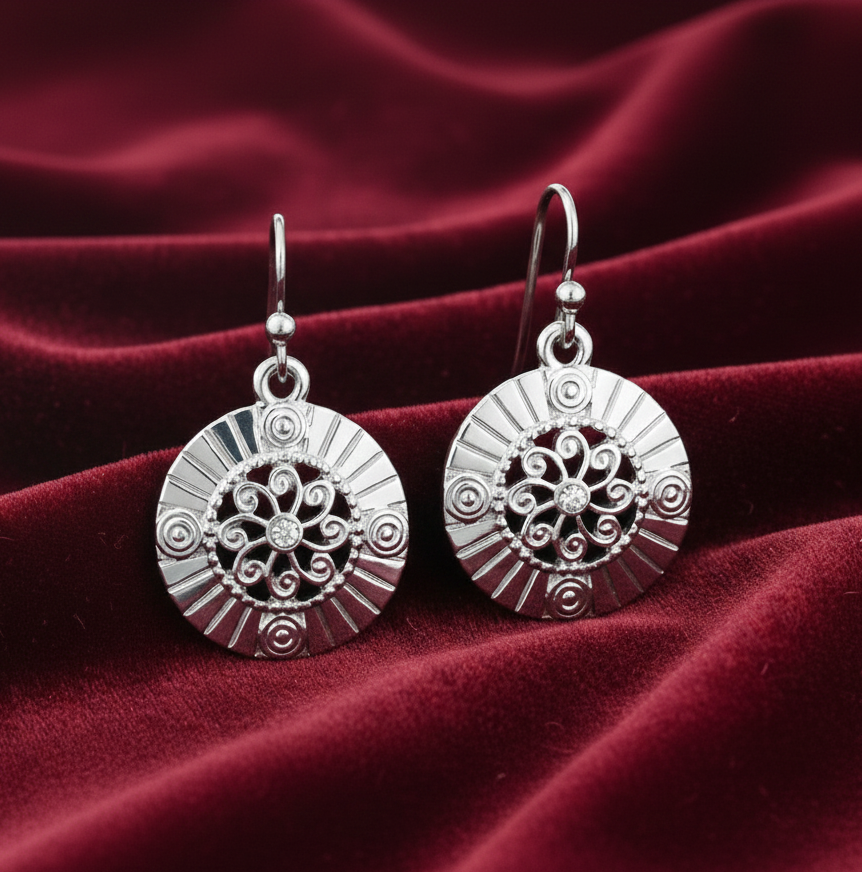 Silver earrings with intricate designs on a red fabric background